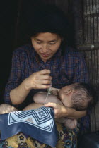 Cambodian refugee mother breastfeeding baby while sewing.