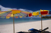 Two multi coloured parasols and  sun loungers on the sandy beach  boat in the distance.   Colored umbrella