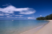 View along the empty sandy beach with a single boat in the blue sea.