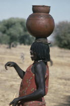 Laughing Chadian refugee woman carrying water pot on her head.