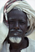 Head and shoulders portrait of Ethiopian refugee man with white beard and turban.