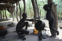 Dinka children cooking over open fire beneath house raised above ground level .