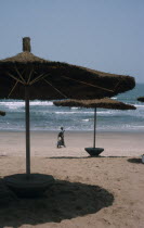 Beach with straw sun shades and a woman with children walking along the sand