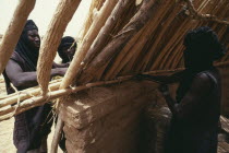 Tuaregs building home using mud bricks and branches for main structure.