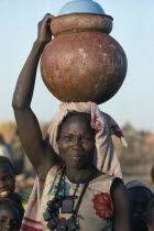 Chadian refugee carrying water pot on her head in camp near El Geneina