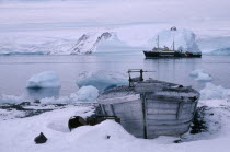 Old whale boat on land with Greenpeace ship in distance.