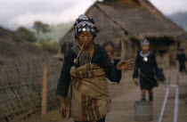 An Akha woman with child strapped to her back  drawing out cotton thread  smoking a pipe. Burma