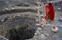 Woman collecting water from open well.