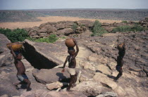 Dogon children carrying water in pots and calabashes on their heads.