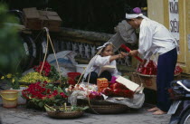 Woman selling religious offerings from the pavement outside a temple