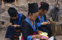 Hmong women in traditional dress doing embroidery.