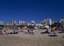 View of beach with people sunbathing and clifftop hotels behind