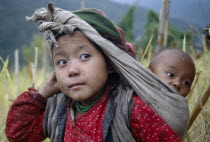 Rai girl carrying baby in sling on her back supported by cloth knotted around head.