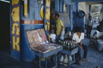 Children and young men outside shop of sweets and drinks vendor with blue and yellow painted exterior.Ayiti Caribbean Haitian Kids Store West Indies Latin America Latino American Immature Male Man Gu...