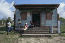 Local store with people standing beside and sitting on steps to entrance.