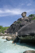 A couple walking in the water at the base of the large rocks.