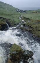 Fast flowing rocky river with village and coastline beyond.