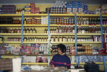 Woman behind counter in general store in front of goods on shelves behind her