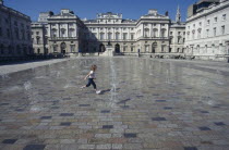 Somerset House and courtyard with rows of small fountains spouting from the ground with a girl running between them.