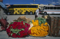 Street scene with large bundles of brightly coloured flowers for Day of the Dead on pavement in the foreground. Colored