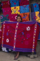 Young girl holding up brightly coloured embroidered local cloth for sale.Colored