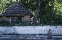 Traditional thatched cottage beside the Larg do Achada the central square with a man sat on the pavement next to a white wall