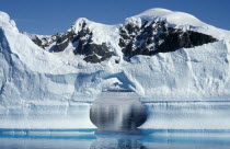 Ice Cliffs with an arch shaped gap in the middle and snow covered mountains behind