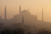 Dome and minarets of Haghia Sophia silhouetted against hazy  pale orange sky amongst rooftops of the Sultanahmet.  Former mosque now museum.EurasiaAya Sofya