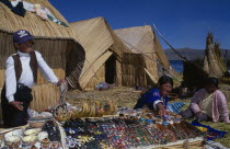 Uros women and young boy selling sounvenirs outside reed houses on a floating island.