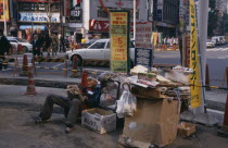 Homeless man living on the street with his cardboard home at a busy road junction