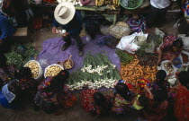 View looking down on market scene with people sitting at a vegetable stall