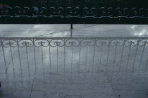 Decorative wrought iron balcony railings casting a shadow onto a pale wet floor.