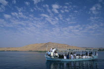 Qubbet el-Hawa and The Tombs of The Nobles with a loaded  passenger ferry sailing past on the river Nile