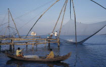 Chinese fishing net being raised with a catch as two men row past in a canoe and a white ship sits on the horizon