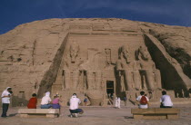 Tourists sitting in front of giant seated statues of Ramesses II at temple entrance