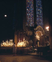 Interior of cathedral showing Notre Dame du Pillar black Madonna beneath stained glass window and women lighting candles.