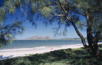 The Bay of Lokaro with view from under trees towards sandy stretch of beach and sea with mountains seen from across the water