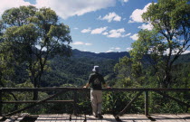 Tourist wearing Madagasgar tshirt standing looking over rantage point towards tropical rainforest