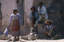 Road to Ranomanfana. Two men sitting on steps at side of building next to two women wearing colourful clothing one selling vegetables