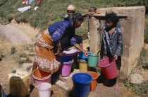 A woman with children collecting water from a nearby public supply point with colourful buckets