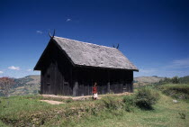 Near Ambositra. Royal wooden hut used by former Malagasy King with a woman standing outside exterior