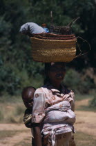 Near Ambositra. Portrait of a woman carrying a baby in a sling on her back and wicker baskets on her head