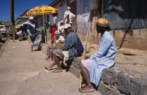 A group of local people sat on a wall waiting at the side of the road