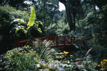 Abbotsbury Sub Tropical Gardens. Red oriental bridge surrounded by exotic plants  trees and flowersEuropean Great Britain Northern Europe UK United Kingdom British Isles