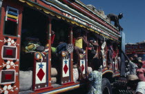 Colourfully painted bus with people loading goods onto the roof