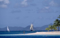 Palm Island Resort. Man walking on sandy outstretch of beach surrounded by turquoise sea with boats on water