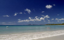 View from the waters edge across calm clear turquoise sea with people swimming in the water and hills seen in the distance