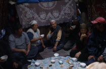 Shepherds inside a yurt  eating and drinking  large rugs hanging on the wallsKyrgyzstan Ger