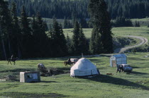 Two men on horses  some standing around a car next to a yurt and small sheds.Kyrgyzstan Tien Shan    Tian Shan  Celestial Mountains. Ger