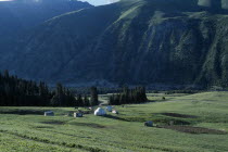 Horses grazing next to small huts on the mountain range.  Kyrgyzstan Tien Shan    Tian Shan  Celestial Mountains.